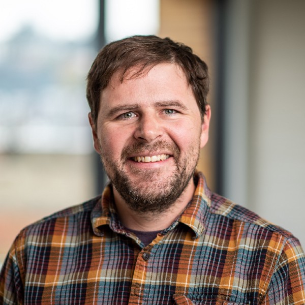 Smiling person wearing plaid with a beard