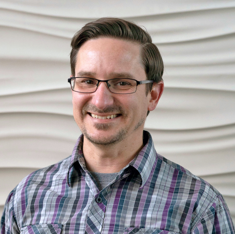 A person smiling wearing glasses wearing plaid