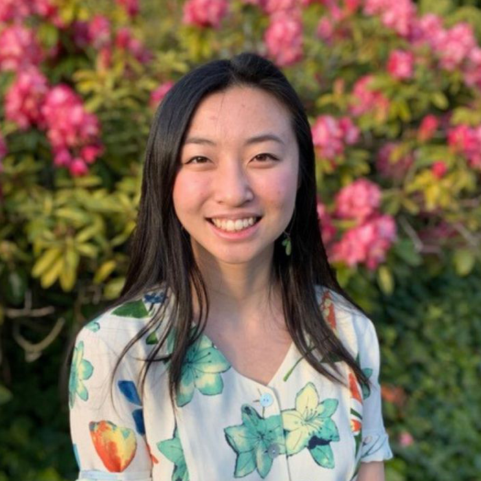 Smiling person with long black hair wearing a water-color patterned blouse