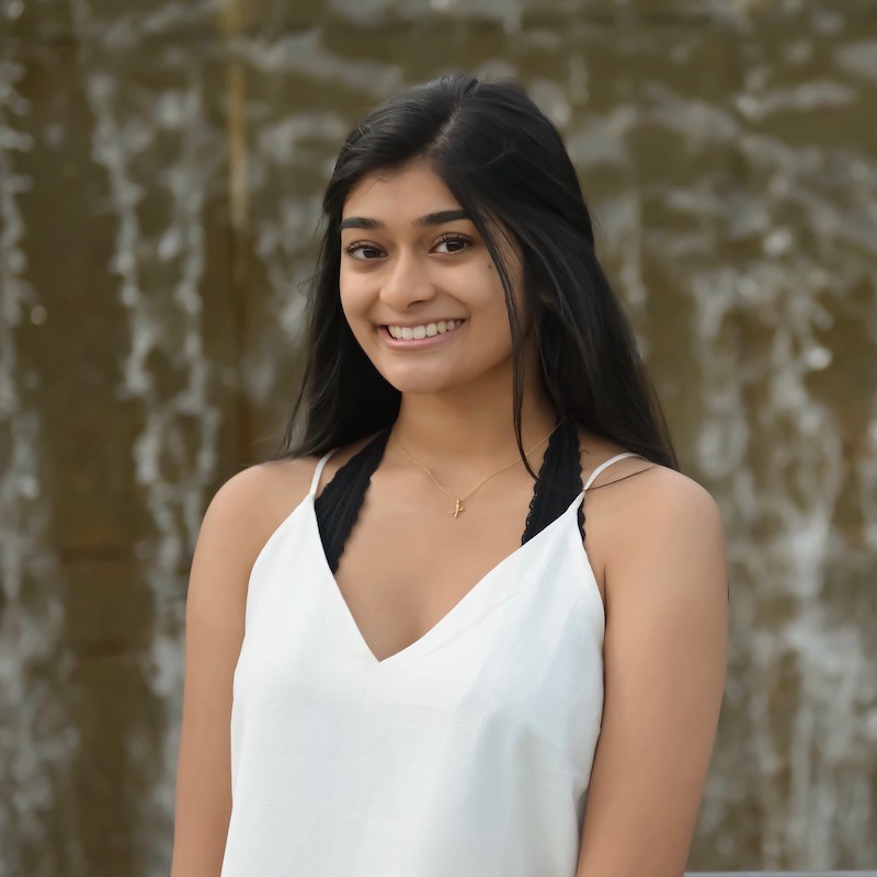 A smiling young person with long black hair wearing a white camisole
