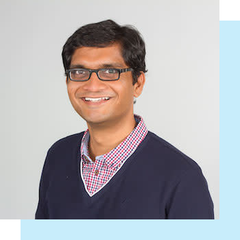 Smiling person with glasses wearing a cardigan over a red plaid shirt