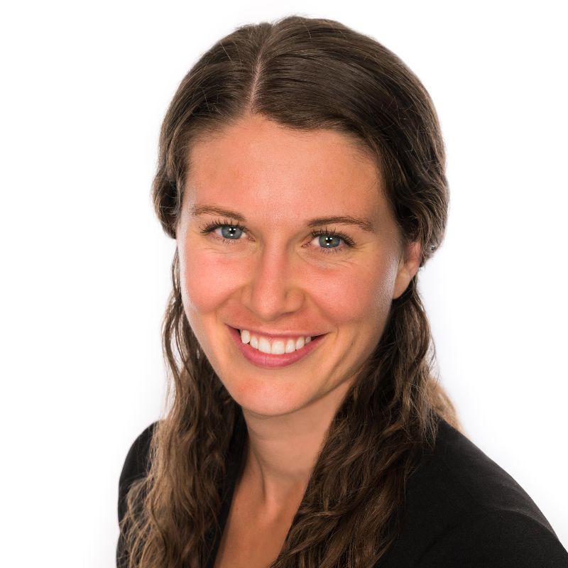 A portrait of Katie Keith, a caucasian woman with long brown hair and blue eyes wearing a black blazer.